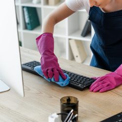 Cleaner in rubber gloves cleaning computer in one of our short term rental home offices